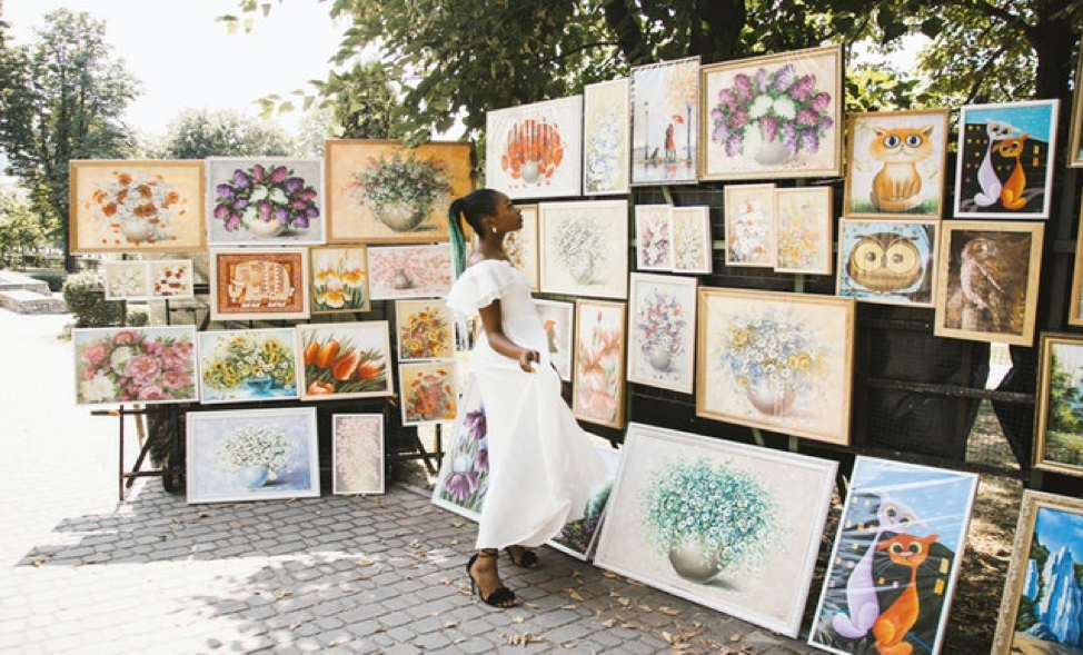 A young woman looking through displayed paintings at an open air gallery.