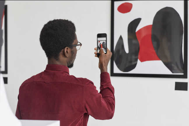 Man taking a photograph of a black and red artwork with his smartphone.